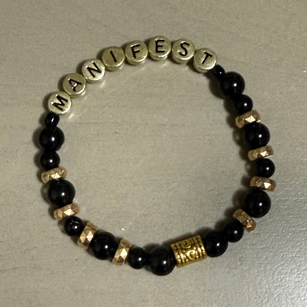 Bracelet with black beads and gold accents on a gray background