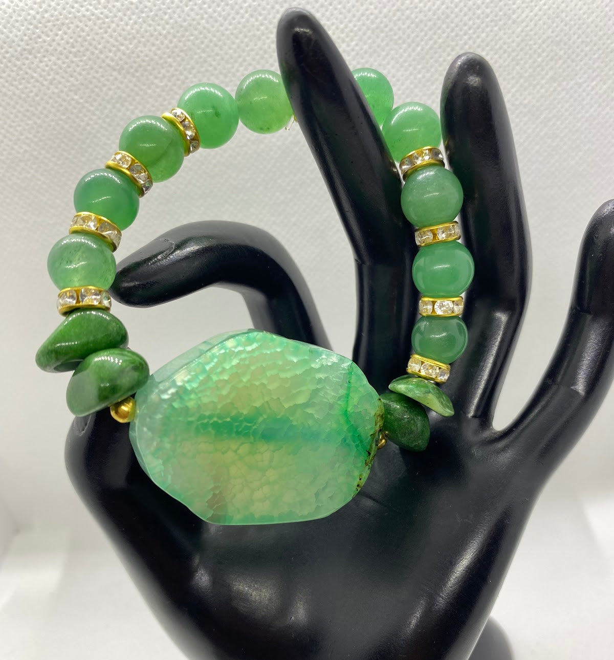 Green beaded bracelet with a large central stone on a black mannequin hand.