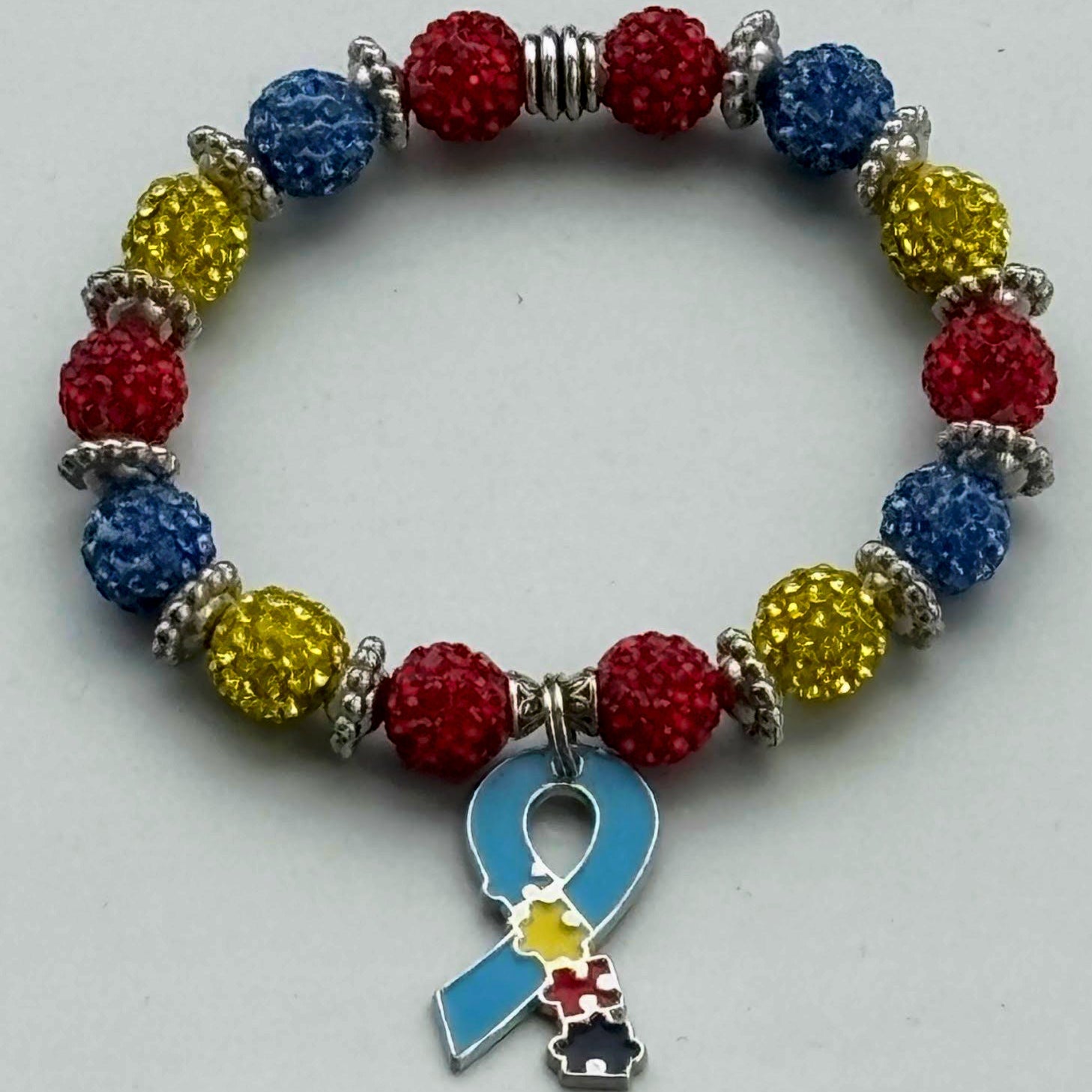 Colorful beaded bracelet with a blue ribbon charm on a gray background