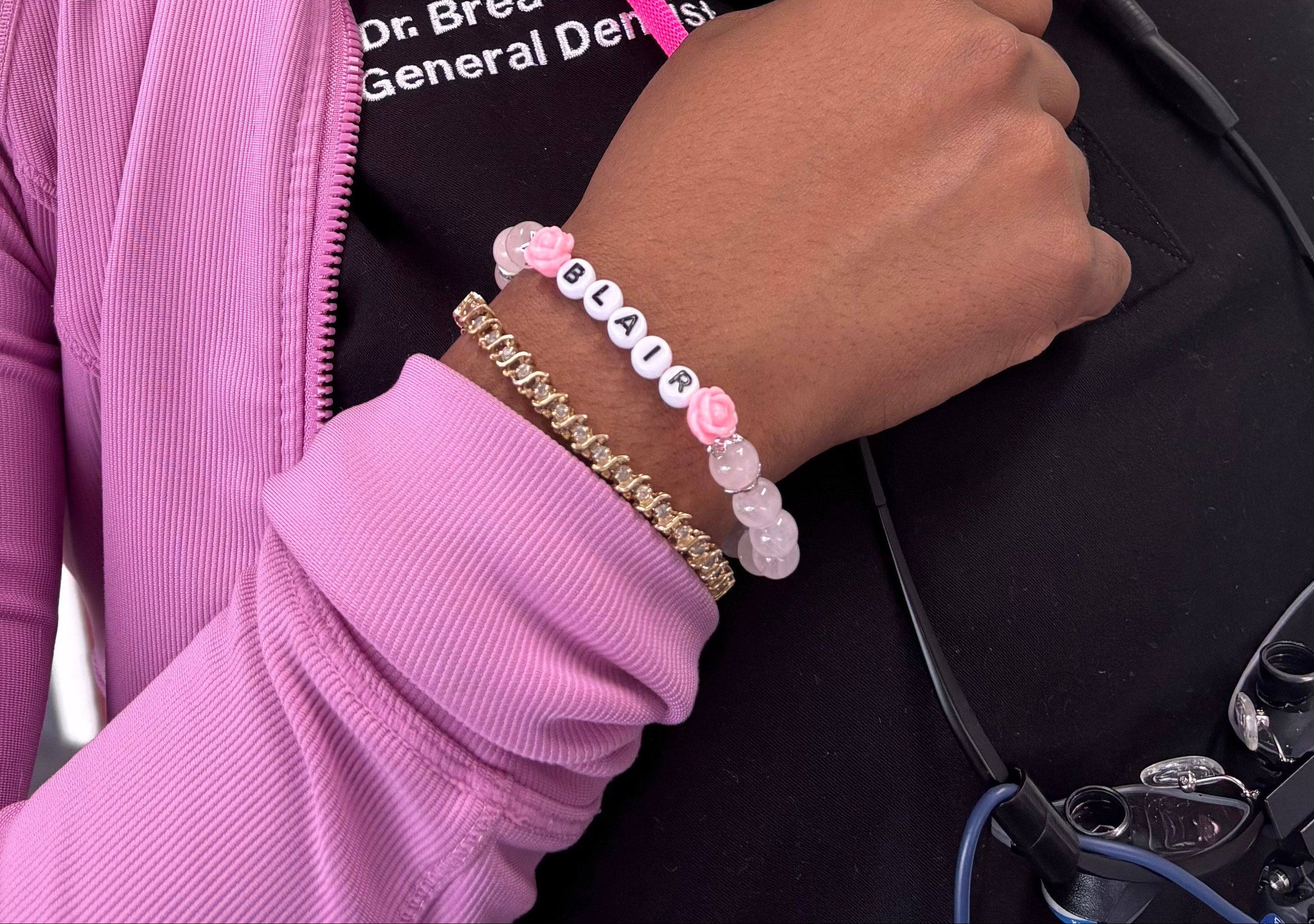 Person wearing a black face mask and pink jacket with a stethoscope, holding a black bag.