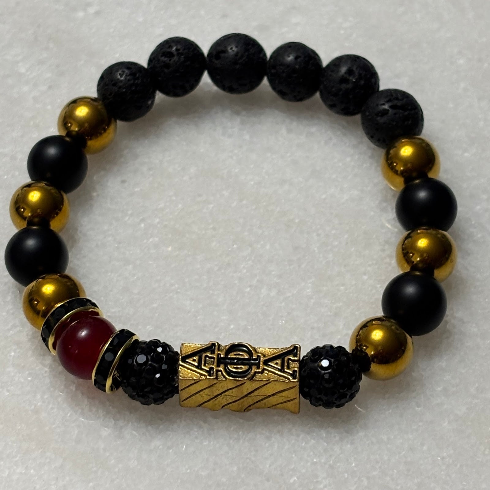Black and gold beaded bracelet with a central decorative element on a light gray background