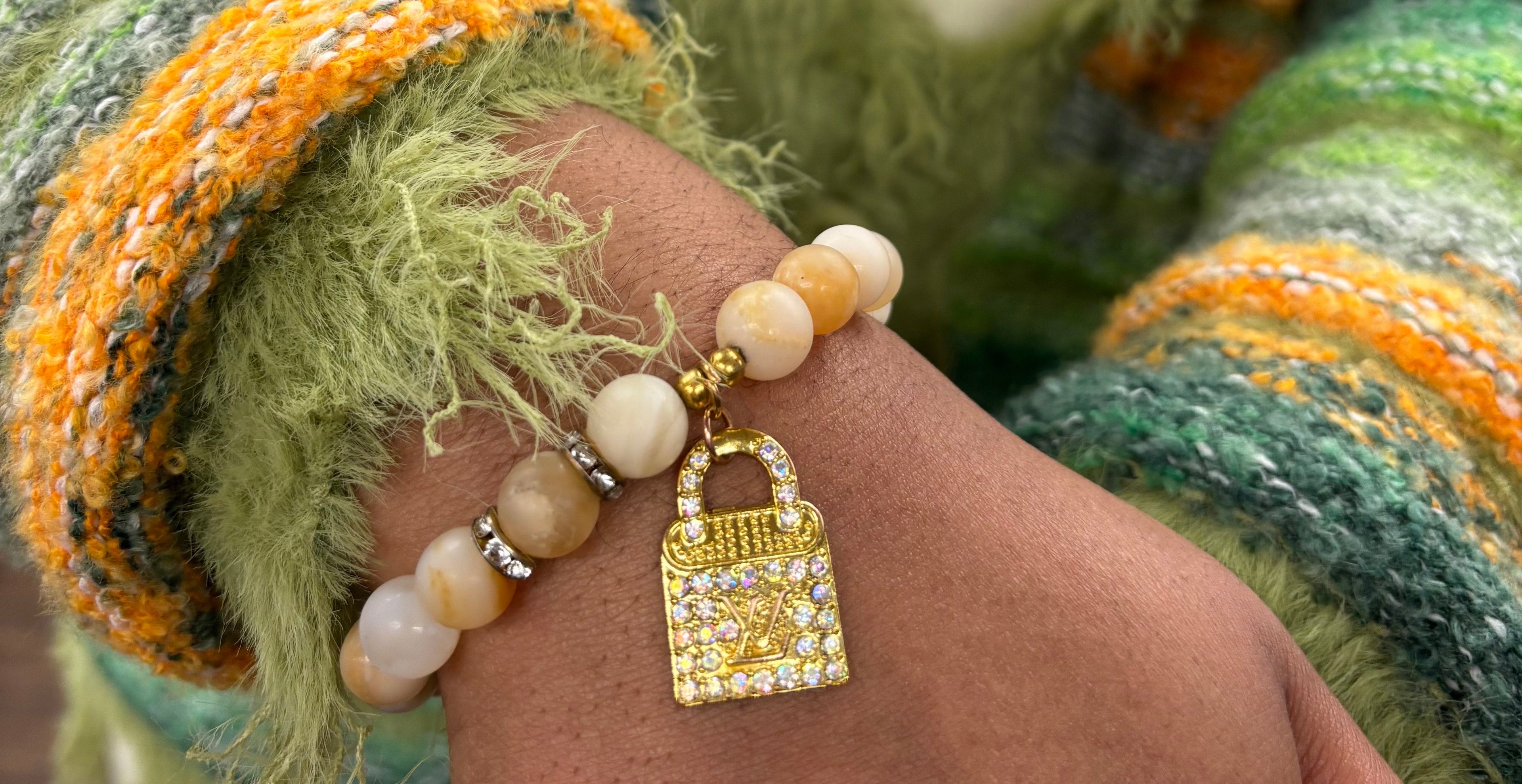 Hand wearing a bracelet with a gold lock charm against a green textured fabric background
