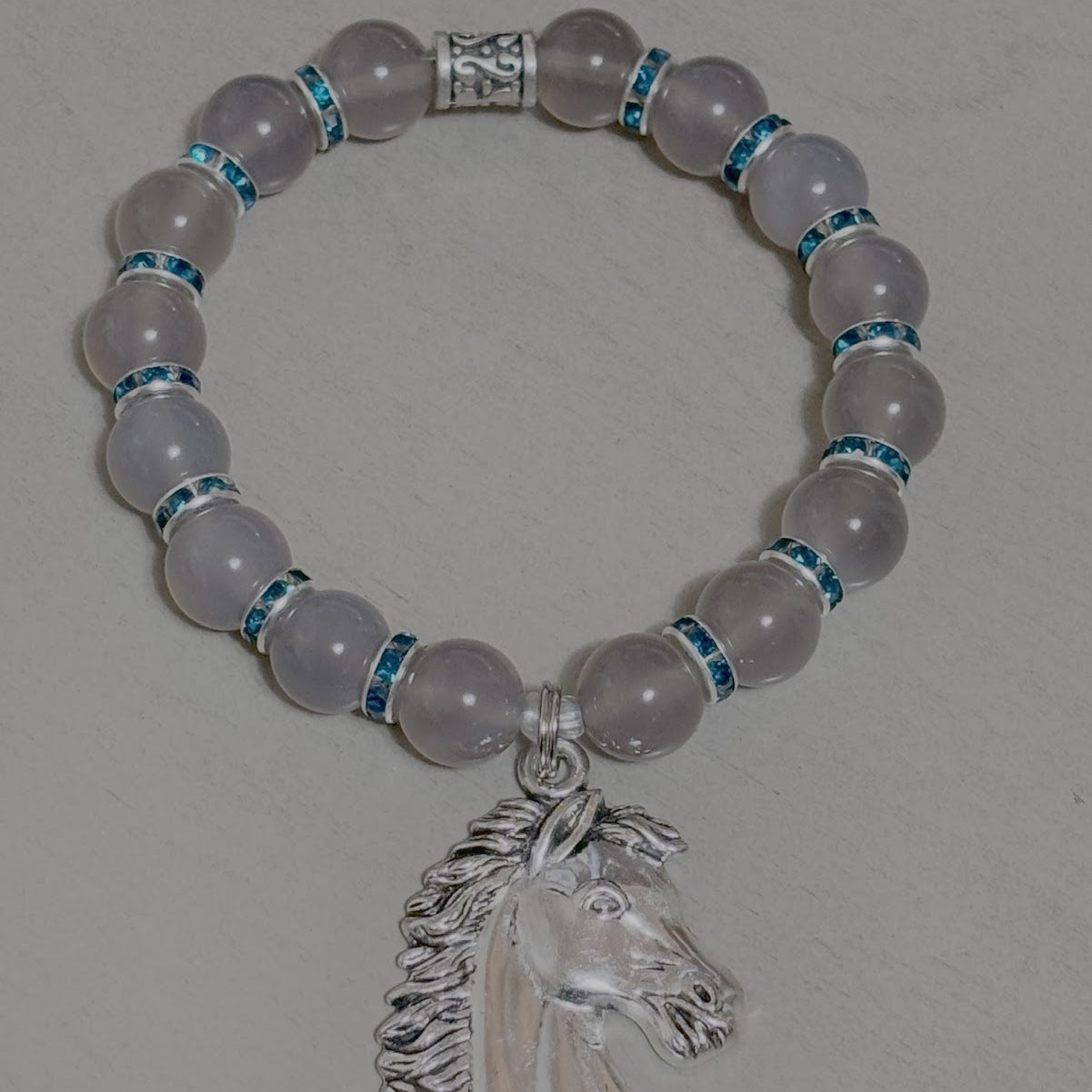 Bracelet with rose quartz beads and a silver horse head charm on a gray background