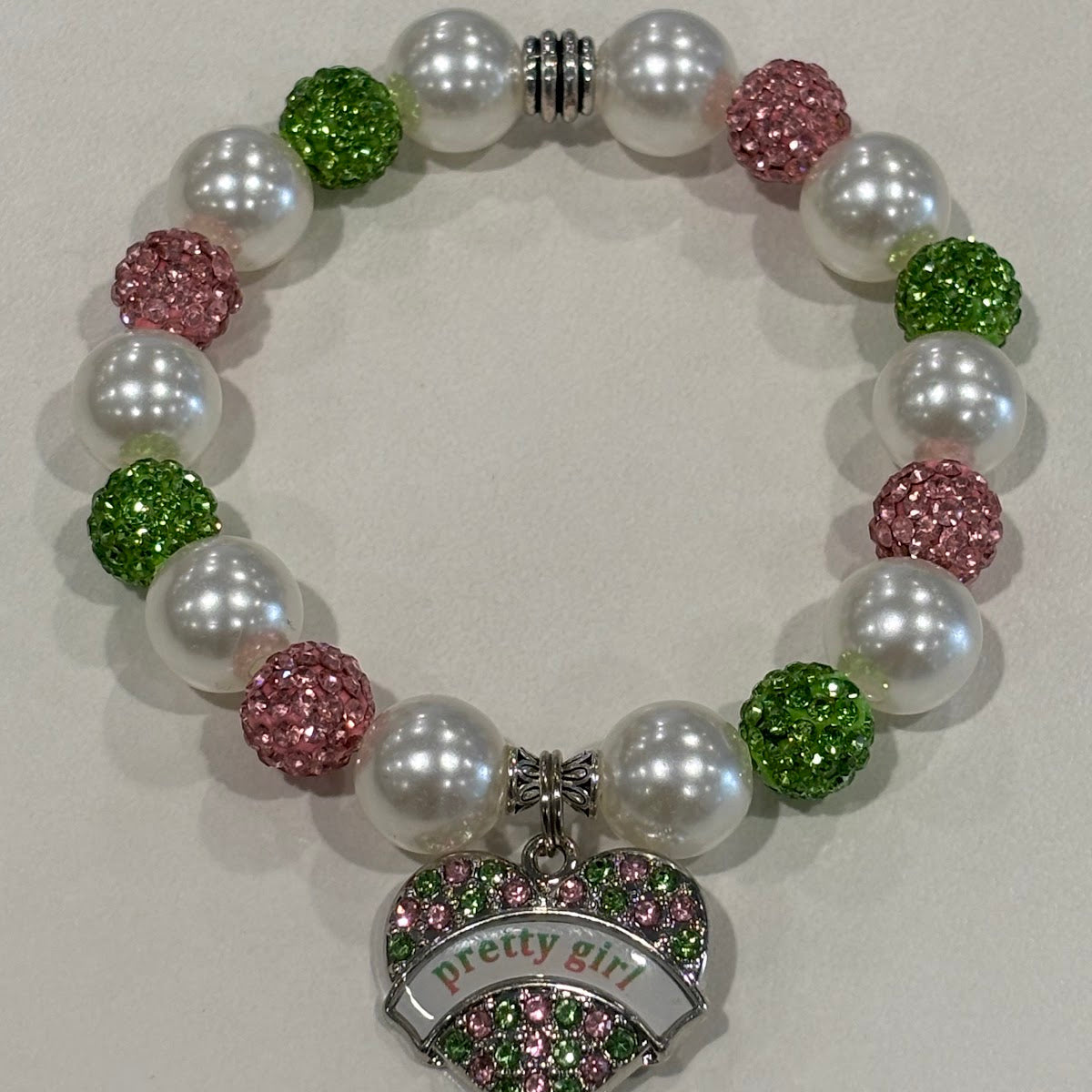 Bracelet with pearls, pink and green beads, and 'pretty girl' heart charm on a light background
