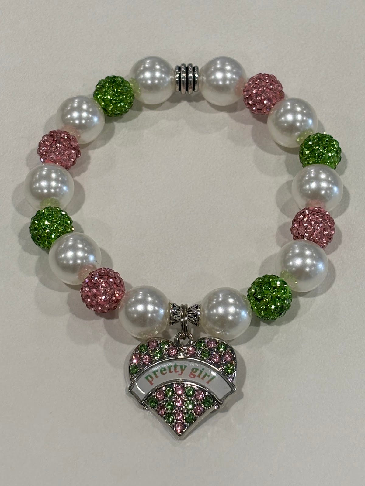 Bracelet with pearls, pink and green beads, and 'pretty girl' heart charm on a light background