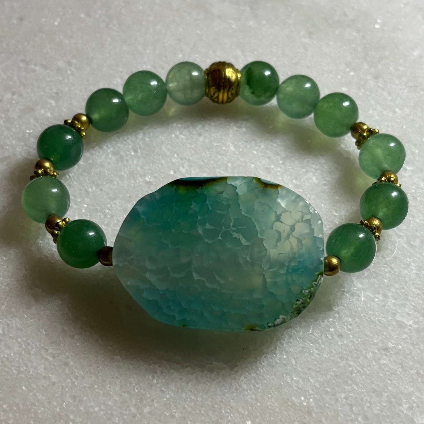 Green beaded bracelet with a large central stone on a light gray background